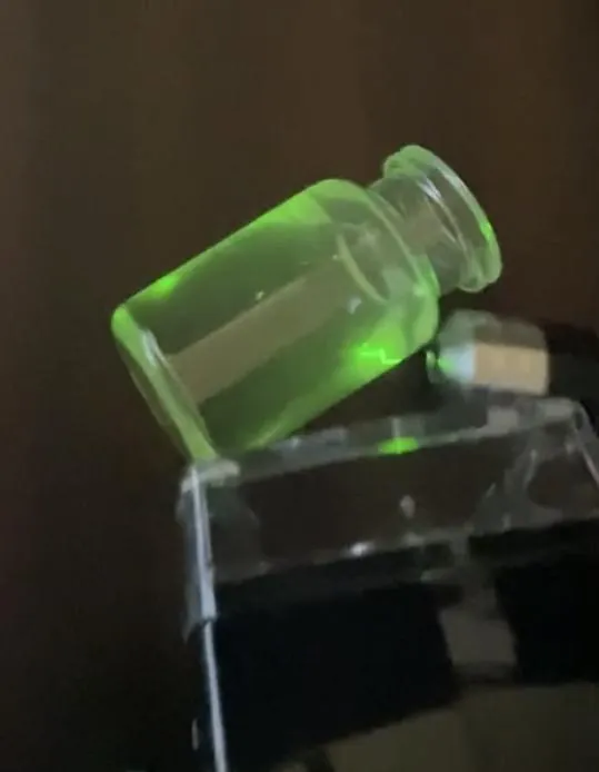 A clear vial glowing green under infrared light because crystals are compounded into its plastic