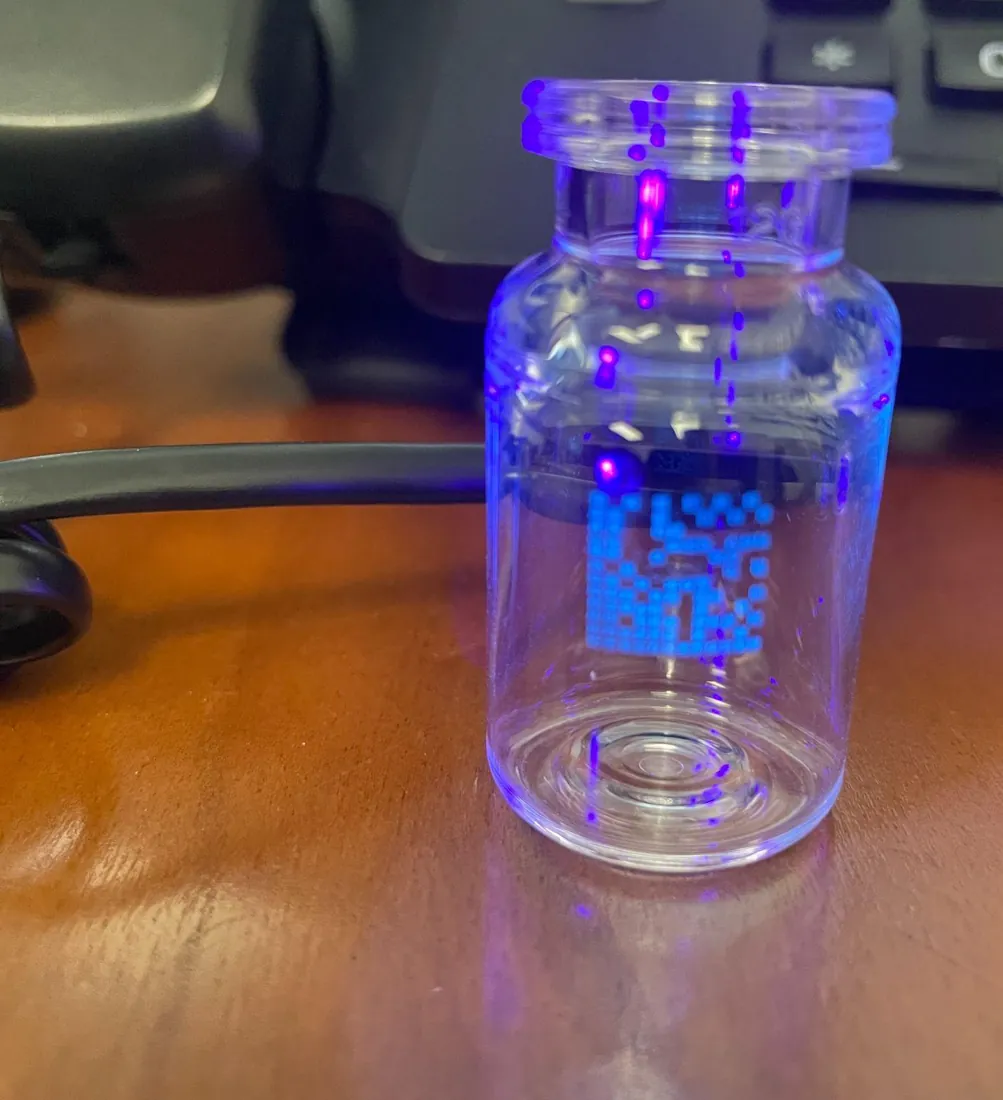 A data-matrix code printed in invisible crystal ink on a clear vial, glowing under UV light